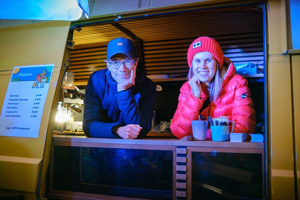 Ein Rotarier und eine Rotaracterin lehnen sich auf die Theke eines Kaffewagens. Auf der Theke steht eine Tasse und eine Sammlung von Zucker-Tüten.