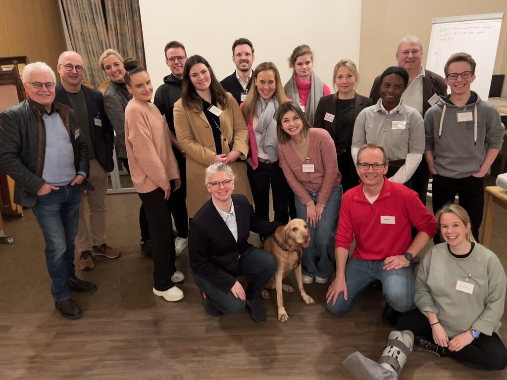 eine Gruppe aus Rotaractern und Rotariern posen für ein Gruppenfoto. In der Mitte sitzt ein sehr süßer Hund.