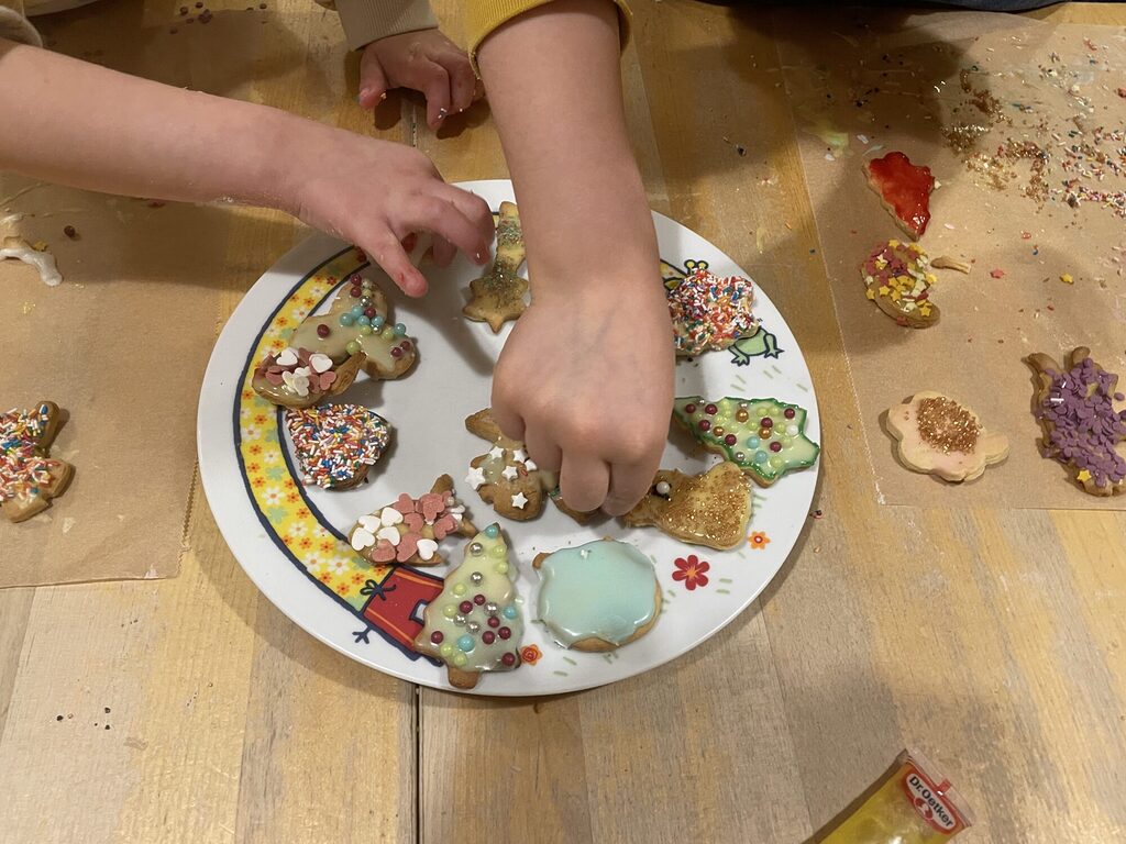 Kinderhände legen mit Zuckerguss dekorierte Plätzchen auf einen Teller