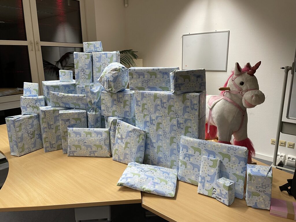 ein großer Stapel eingepackter Geschenke und ein pink-weißes Schaukel-Einhorn liegen auf einem Tisch