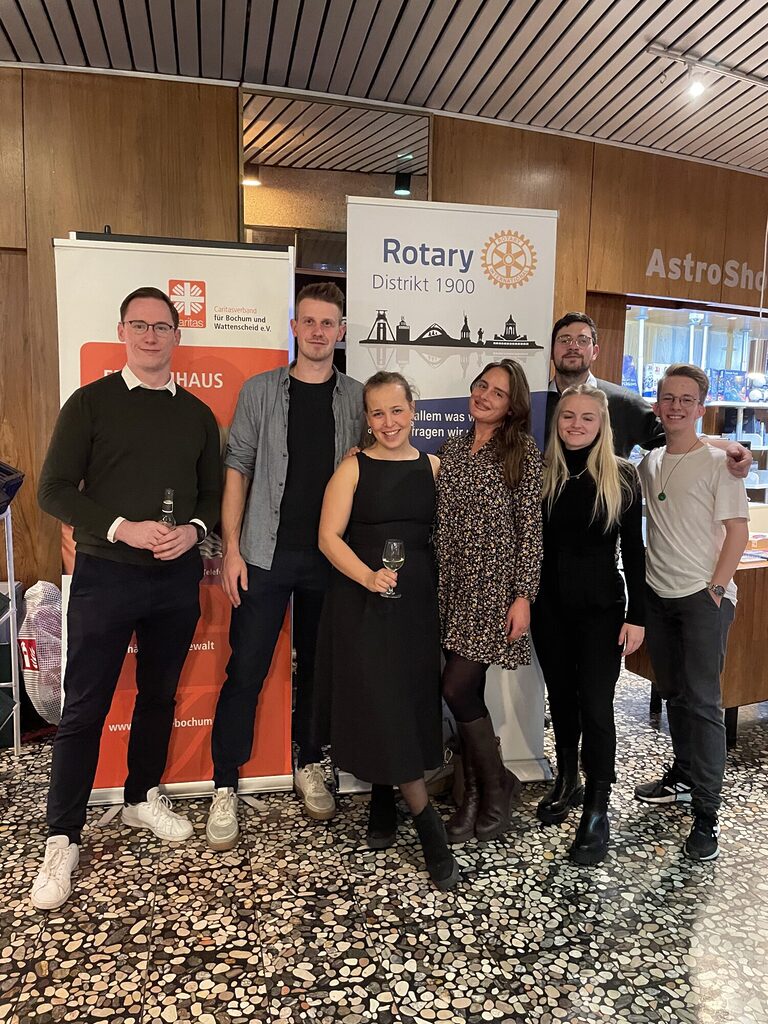 Sieben Rotaracter stehen im Planetarium Bochum und gucken in die Kamera. Im Hintergrund sind Roll-ups der rotarischen Familie in Bochum zu erkennen.